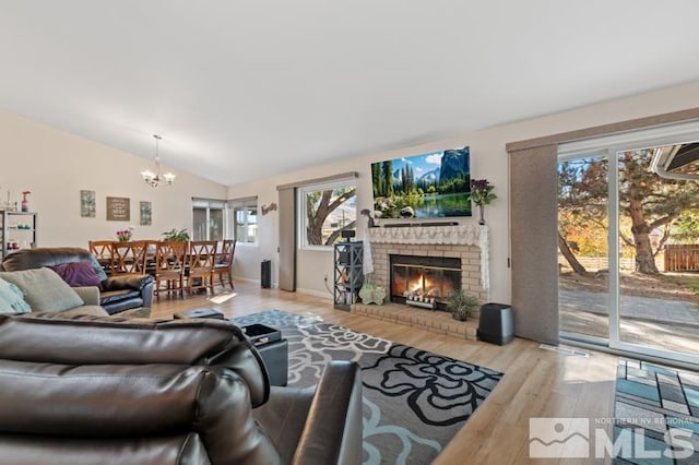 living room with light hardwood / wood-style floors, lofted ceiling, an inviting chandelier, and a fireplace