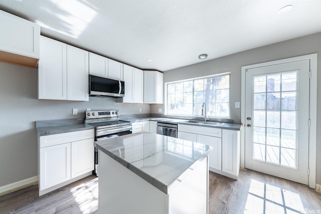 kitchen featuring appliances with stainless steel finishes, white cabinetry, light hardwood / wood-style flooring, sink, and a center island