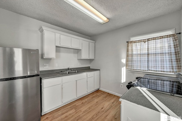 kitchen featuring sink, a textured ceiling, stainless steel fridge, light hardwood / wood-style floors, and white cabinets