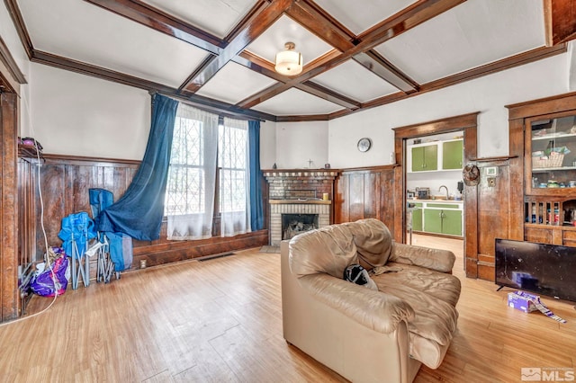 living room featuring wood walls, light wood-type flooring, a brick fireplace, coffered ceiling, and beam ceiling