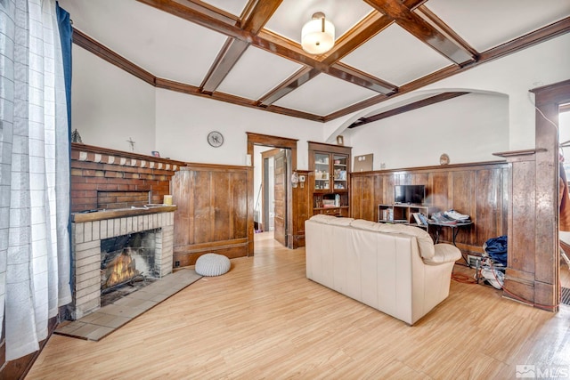 living room featuring a brick fireplace, light hardwood / wood-style floors, coffered ceiling, beamed ceiling, and wooden walls