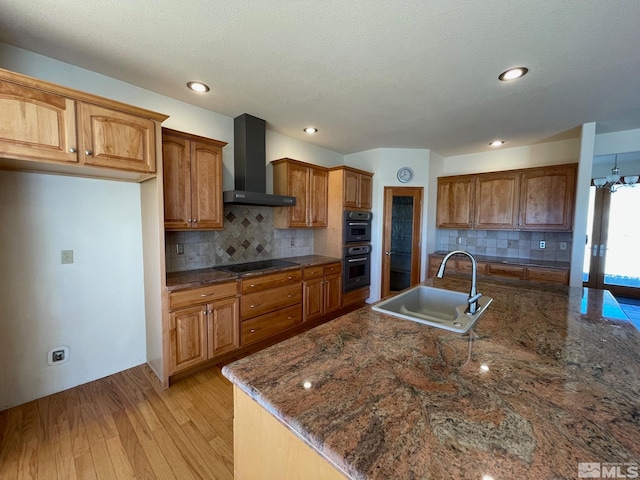 kitchen with wall chimney exhaust hood, sink, light hardwood / wood-style flooring, and tasteful backsplash