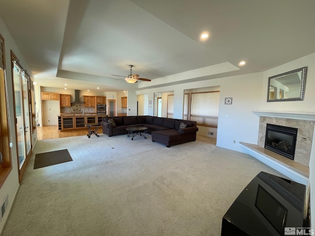 carpeted living room featuring a fireplace, a tray ceiling, and ceiling fan