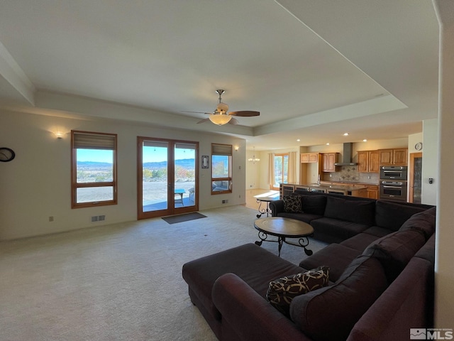 carpeted living room with a tray ceiling and ceiling fan