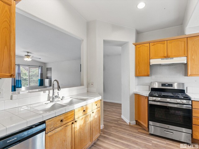 kitchen featuring ceiling fan, light hardwood / wood-style flooring, sink, tile counters, and stainless steel appliances