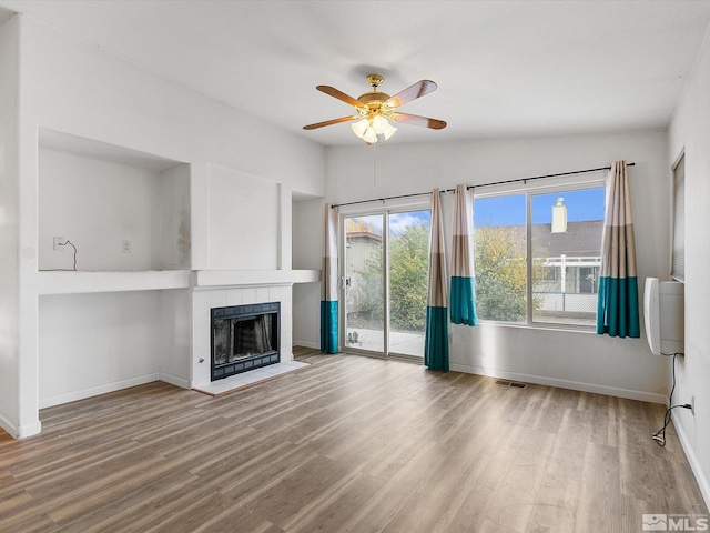 unfurnished living room featuring wood-type flooring, a wall mounted air conditioner, a tile fireplace, ceiling fan, and vaulted ceiling