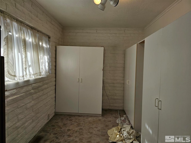 unfurnished bedroom with brick wall, a textured ceiling, carpet flooring, and ceiling fan