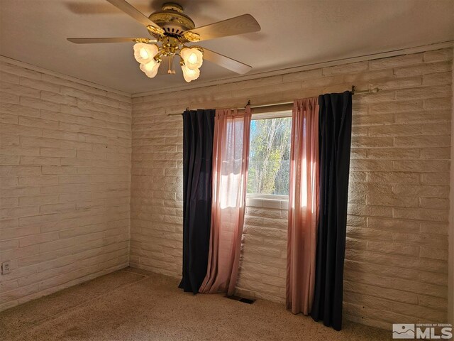 carpeted empty room with ceiling fan and brick wall