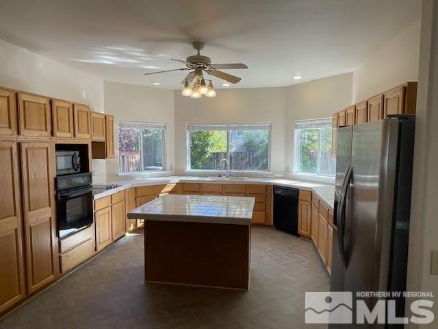 kitchen featuring a kitchen island, black appliances, tile countertops, and a healthy amount of sunlight