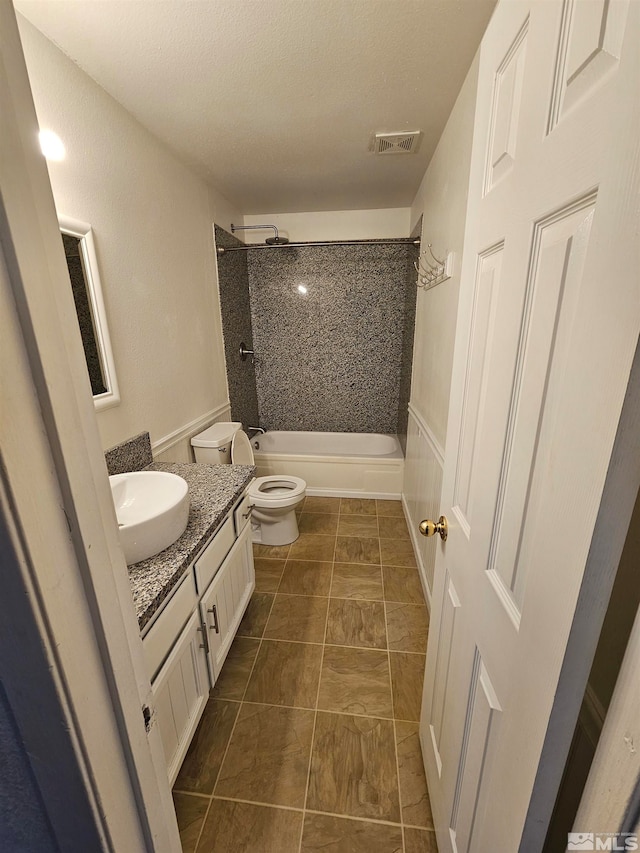 full bathroom with vanity, a textured ceiling, tiled shower / bath combo, tile patterned flooring, and toilet