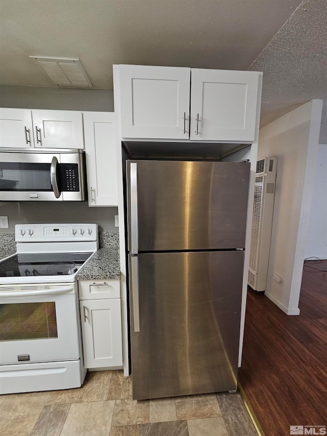 kitchen with light hardwood / wood-style floors, white cabinets, a textured ceiling, stone counters, and appliances with stainless steel finishes