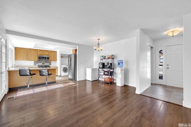 kitchen with washer / dryer, stainless steel appliances, dark hardwood / wood-style floors, a breakfast bar area, and kitchen peninsula