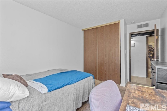 bedroom with light colored carpet, a textured ceiling, and a closet