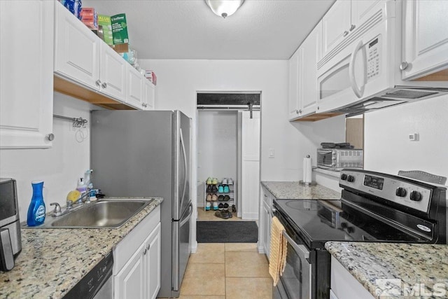 kitchen with sink, light tile patterned flooring, light stone counters, white cabinetry, and stainless steel appliances