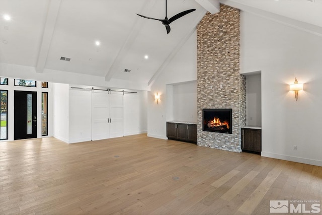 unfurnished living room featuring a stone fireplace, light wood-type flooring, a barn door, and high vaulted ceiling