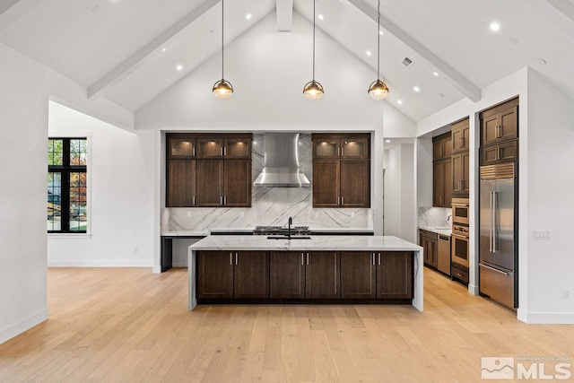 kitchen featuring decorative backsplash, wall chimney range hood, beam ceiling, light wood-type flooring, and appliances with stainless steel finishes