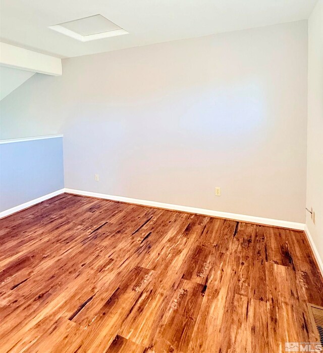 spare room featuring wood-type flooring and lofted ceiling with beams