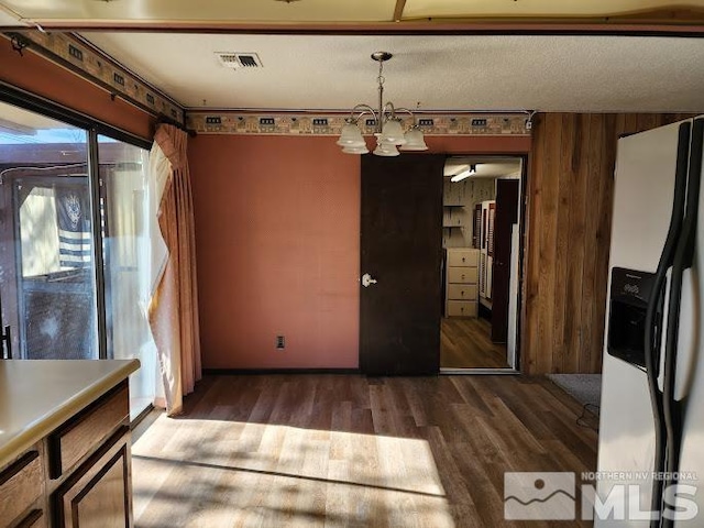 unfurnished dining area with dark wood-type flooring, wood walls, and an inviting chandelier