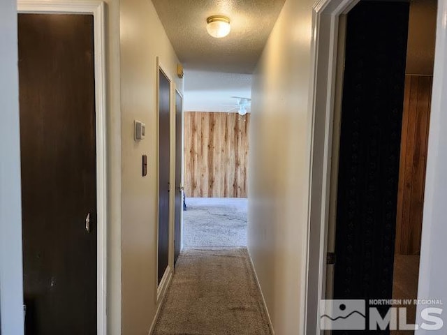 hall featuring carpet flooring, wood walls, and a textured ceiling