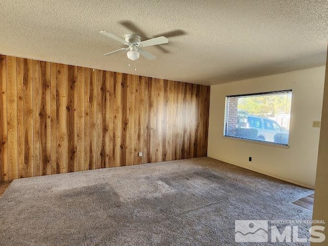 carpeted empty room with wood walls, a textured ceiling, and ceiling fan