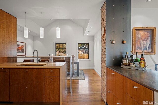 kitchen with high vaulted ceiling, light hardwood / wood-style flooring, hanging light fixtures, and sink