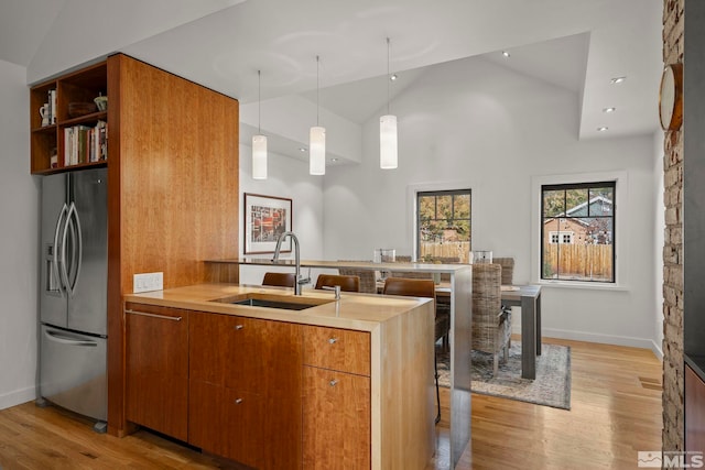 kitchen with light hardwood / wood-style floors, hanging light fixtures, sink, stainless steel fridge with ice dispenser, and high vaulted ceiling