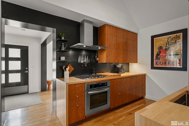 kitchen featuring stainless steel appliances, lofted ceiling, wall chimney range hood, backsplash, and light wood-type flooring