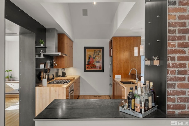 kitchen with stainless steel appliances, light hardwood / wood-style flooring, sink, wall chimney exhaust hood, and brick wall