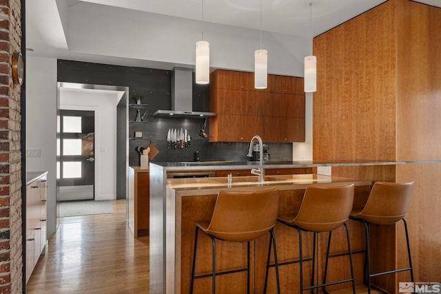 kitchen with brick wall, tasteful backsplash, decorative light fixtures, wood-type flooring, and wall chimney range hood