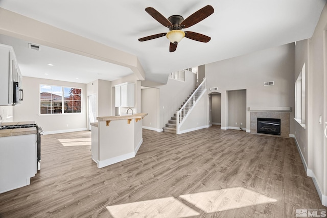 unfurnished living room with light wood-type flooring, a tiled fireplace, and ceiling fan