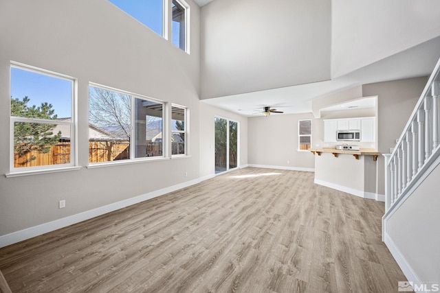 unfurnished living room featuring a towering ceiling, light wood-type flooring, and ceiling fan