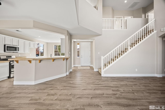 kitchen with kitchen peninsula, appliances with stainless steel finishes, a kitchen breakfast bar, white cabinets, and light wood-type flooring