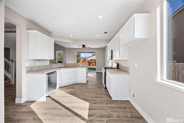 kitchen with stainless steel appliances, kitchen peninsula, sink, white cabinetry, and light wood-type flooring