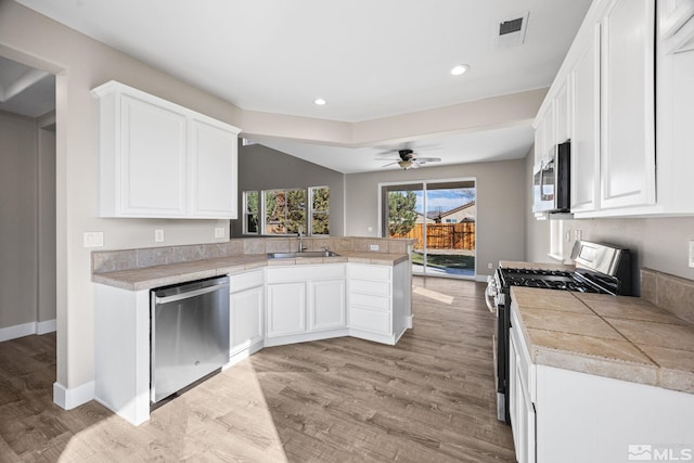 kitchen featuring stainless steel appliances, white cabinetry, sink, kitchen peninsula, and light hardwood / wood-style flooring