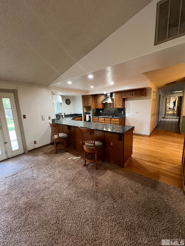 bar featuring lofted ceiling, wall chimney range hood, a textured ceiling, tasteful backsplash, and light hardwood / wood-style floors