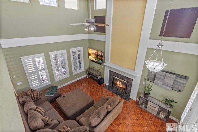 living room with a fireplace, a towering ceiling, and ceiling fan with notable chandelier