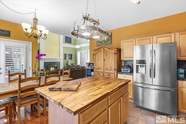 kitchen featuring butcher block counters, stainless steel refrigerator with ice dispenser, a kitchen island, backsplash, and a high end fireplace