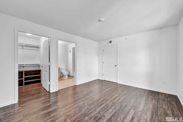 unfurnished bedroom featuring dark hardwood / wood-style flooring, a closet, a walk in closet, and ensuite bathroom