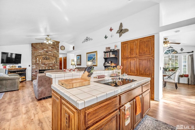 kitchen featuring light wood-type flooring, tile countertops, vaulted ceiling, and black electric stovetop