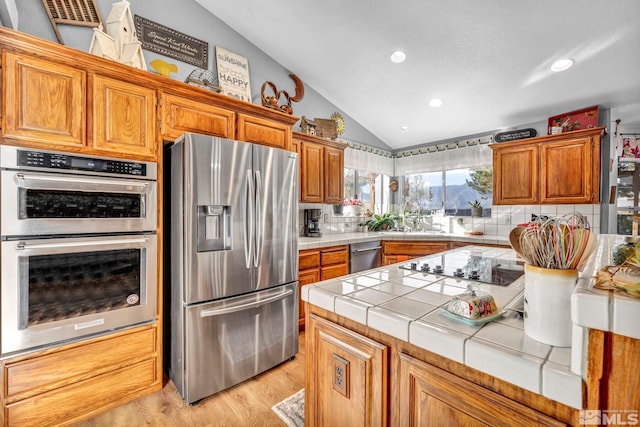 kitchen featuring tile counters, stainless steel appliances, light hardwood / wood-style floors, vaulted ceiling, and backsplash