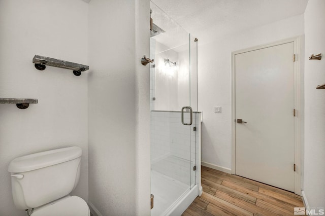 bathroom with a textured ceiling, hardwood / wood-style flooring, toilet, and a shower with door