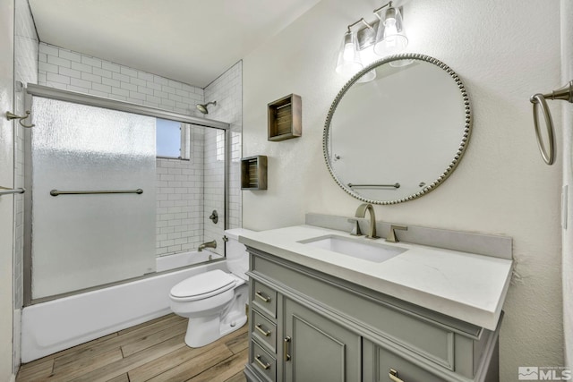 full bathroom with hardwood / wood-style floors, bath / shower combo with glass door, vanity, and toilet