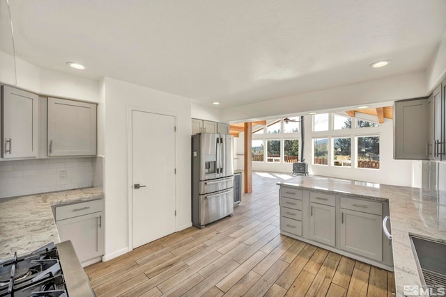 kitchen with gray cabinetry, tasteful backsplash, light stone counters, stainless steel fridge, and light hardwood / wood-style flooring