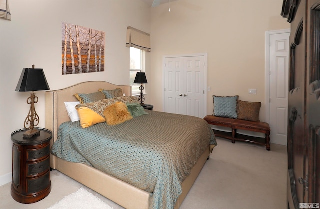 bedroom featuring ceiling fan, a closet, a towering ceiling, and light colored carpet