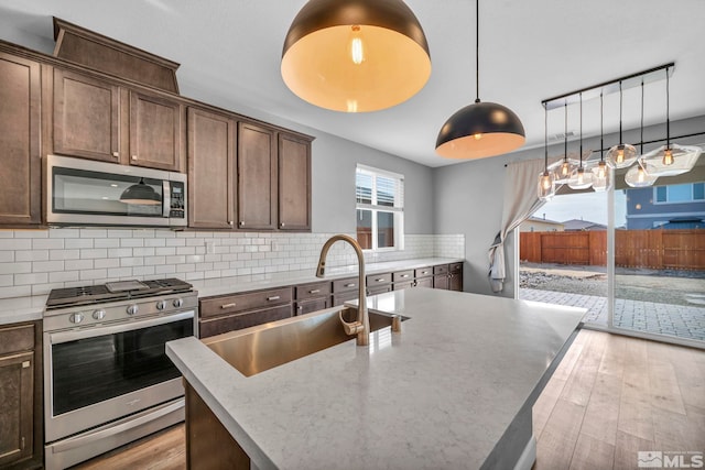 kitchen with appliances with stainless steel finishes, hanging light fixtures, light hardwood / wood-style floors, and an island with sink