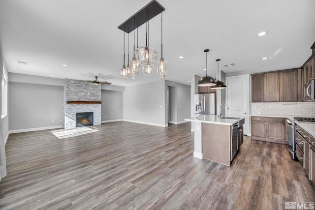 kitchen with hardwood / wood-style floors, appliances with stainless steel finishes, hanging light fixtures, and a center island with sink