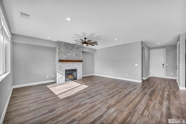 unfurnished living room with a stone fireplace, dark hardwood / wood-style floors, and ceiling fan