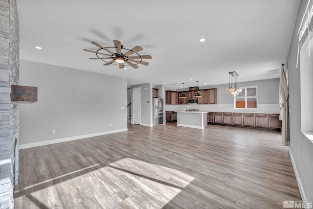 unfurnished living room with light wood-type flooring and ceiling fan with notable chandelier