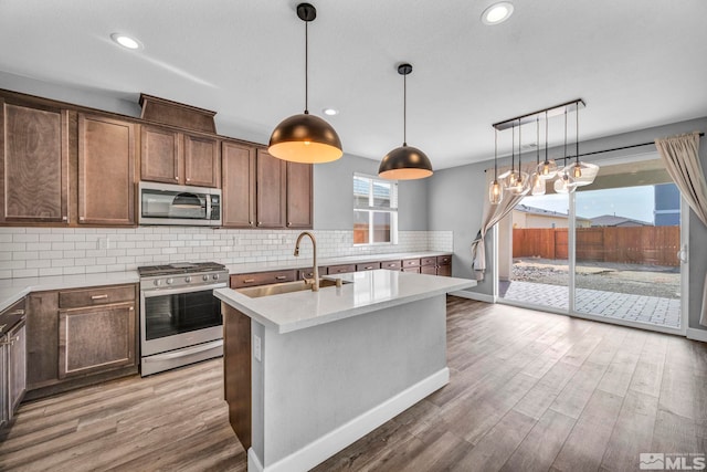 kitchen with stainless steel appliances, a center island with sink, decorative light fixtures, and dark hardwood / wood-style flooring