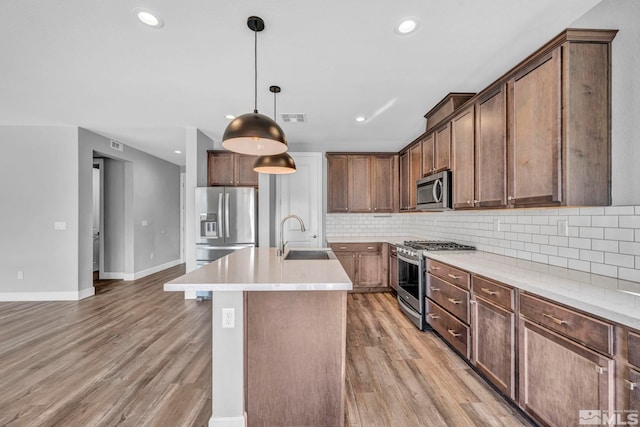 kitchen featuring wood-type flooring, sink, a kitchen island with sink, appliances with stainless steel finishes, and decorative light fixtures